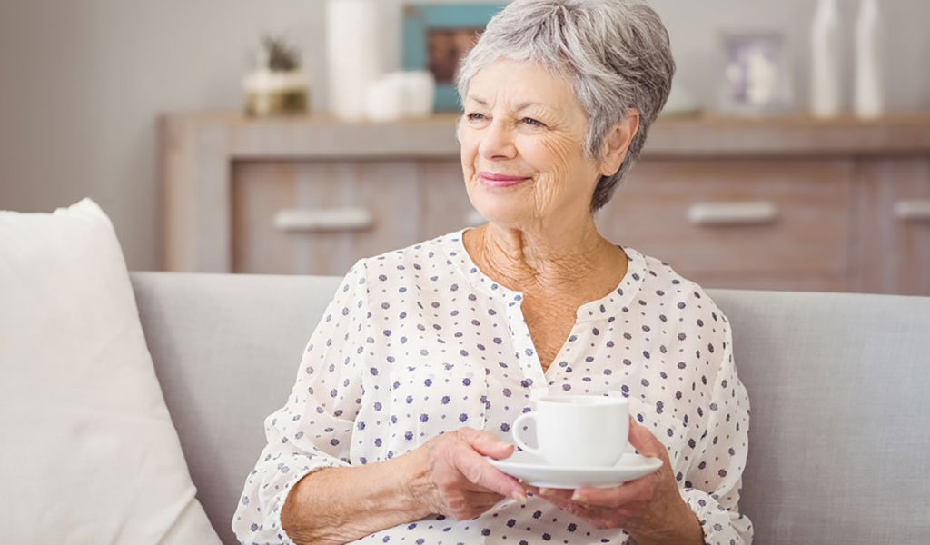 Glückliche Frau trinkt Kaffee auf Sofa