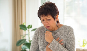 Frau hustet kräftig und hält sich beide Hände vor die Brust