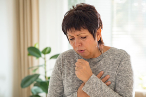 Frau hustet kräftig und hält sich beide Hände vor die Brust