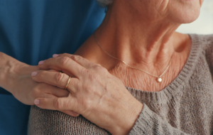 Eine Person legt sanft ihre Hand auf die Schulter einer älteren Frau und bietet ihr Trost und Unterstützung.